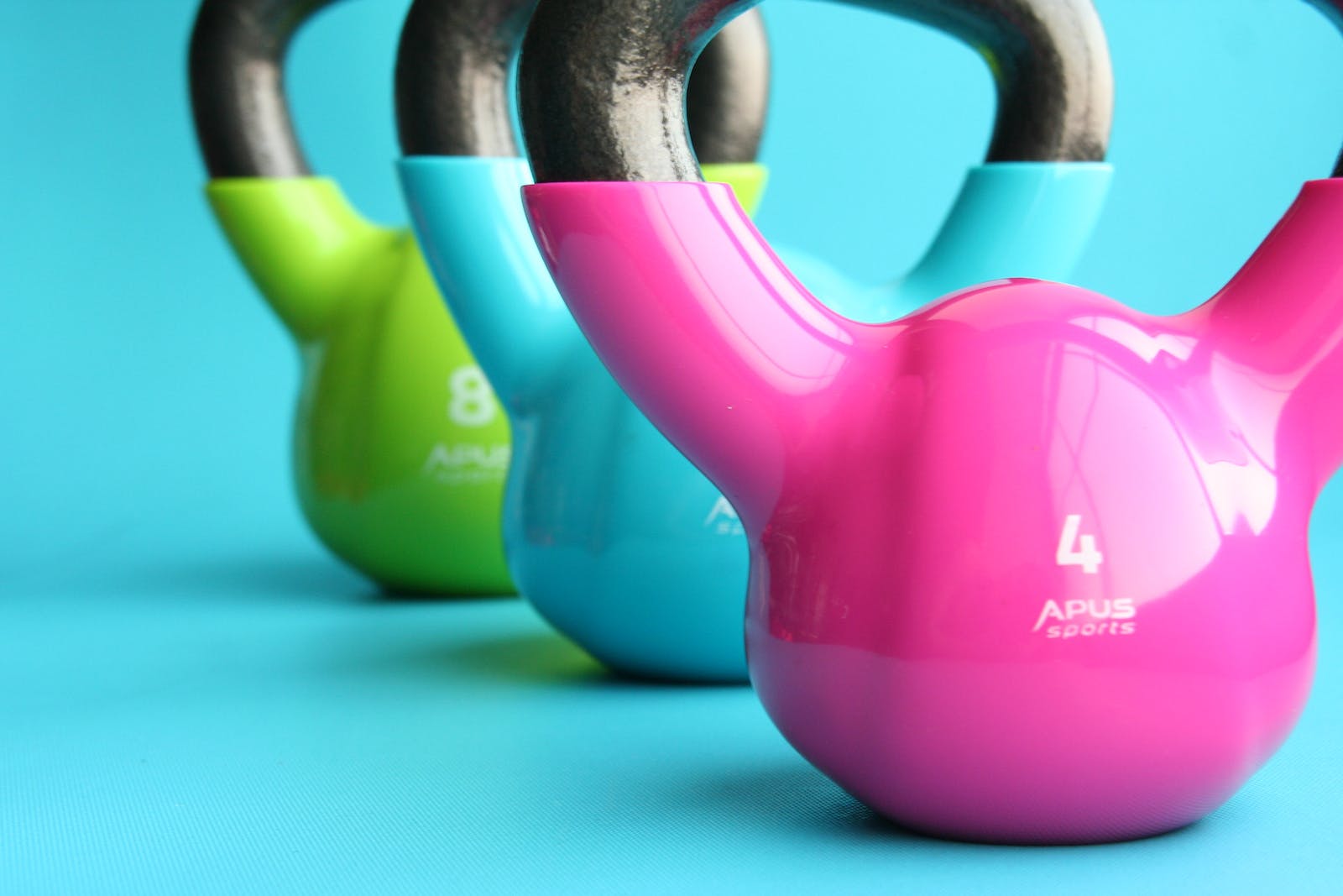 Green, Blue, and Pink Kettle Bells on Blue Surface